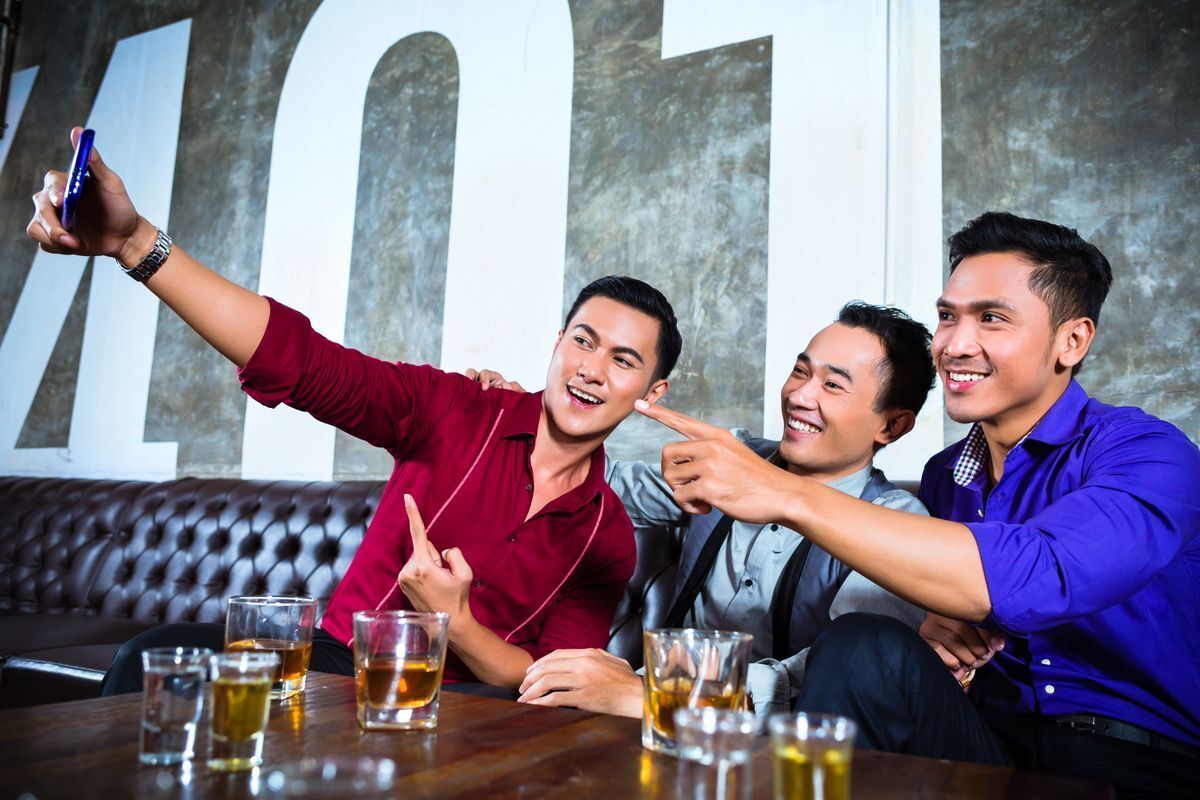 Asian guys in a bar taking a photo of themselves smiling.