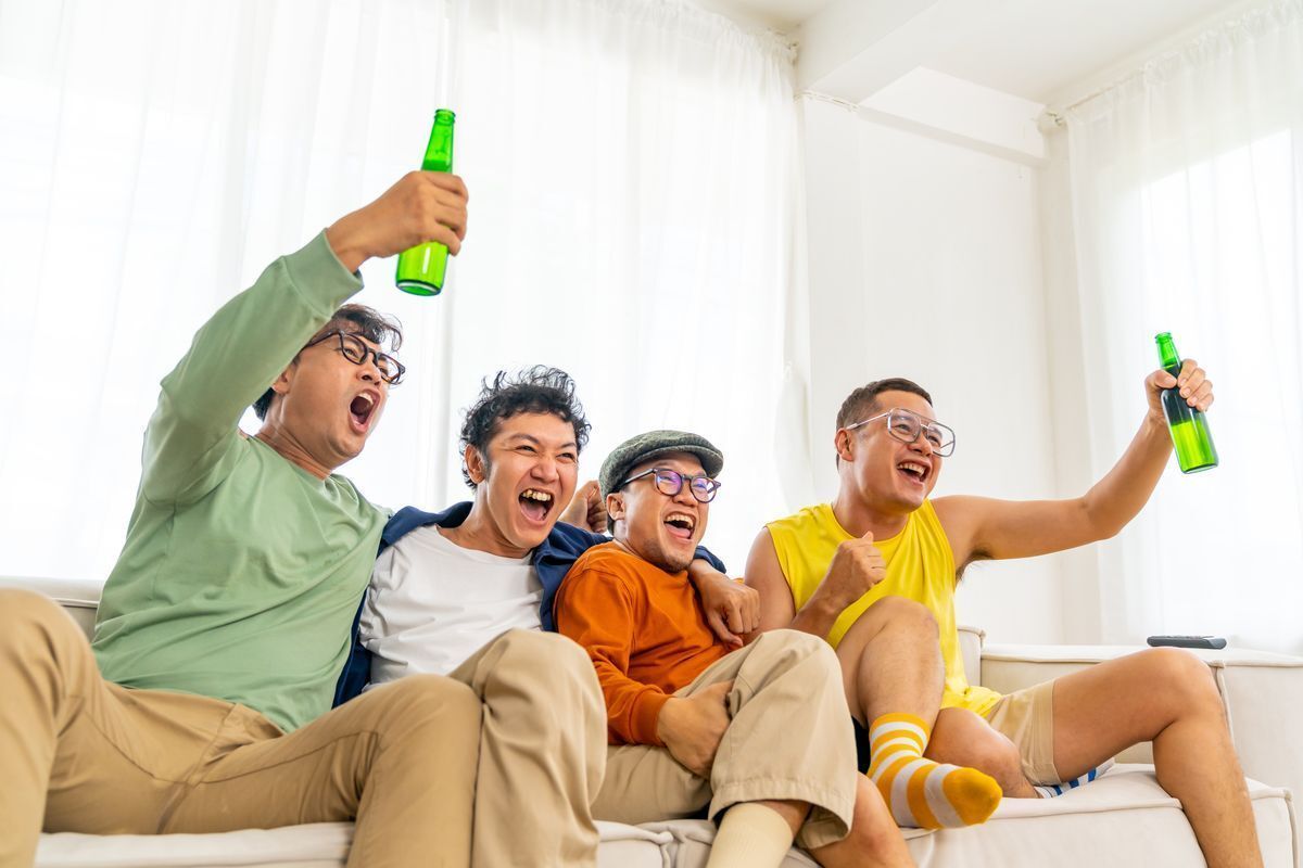A group of men cheering on a sofa with beers in hands.