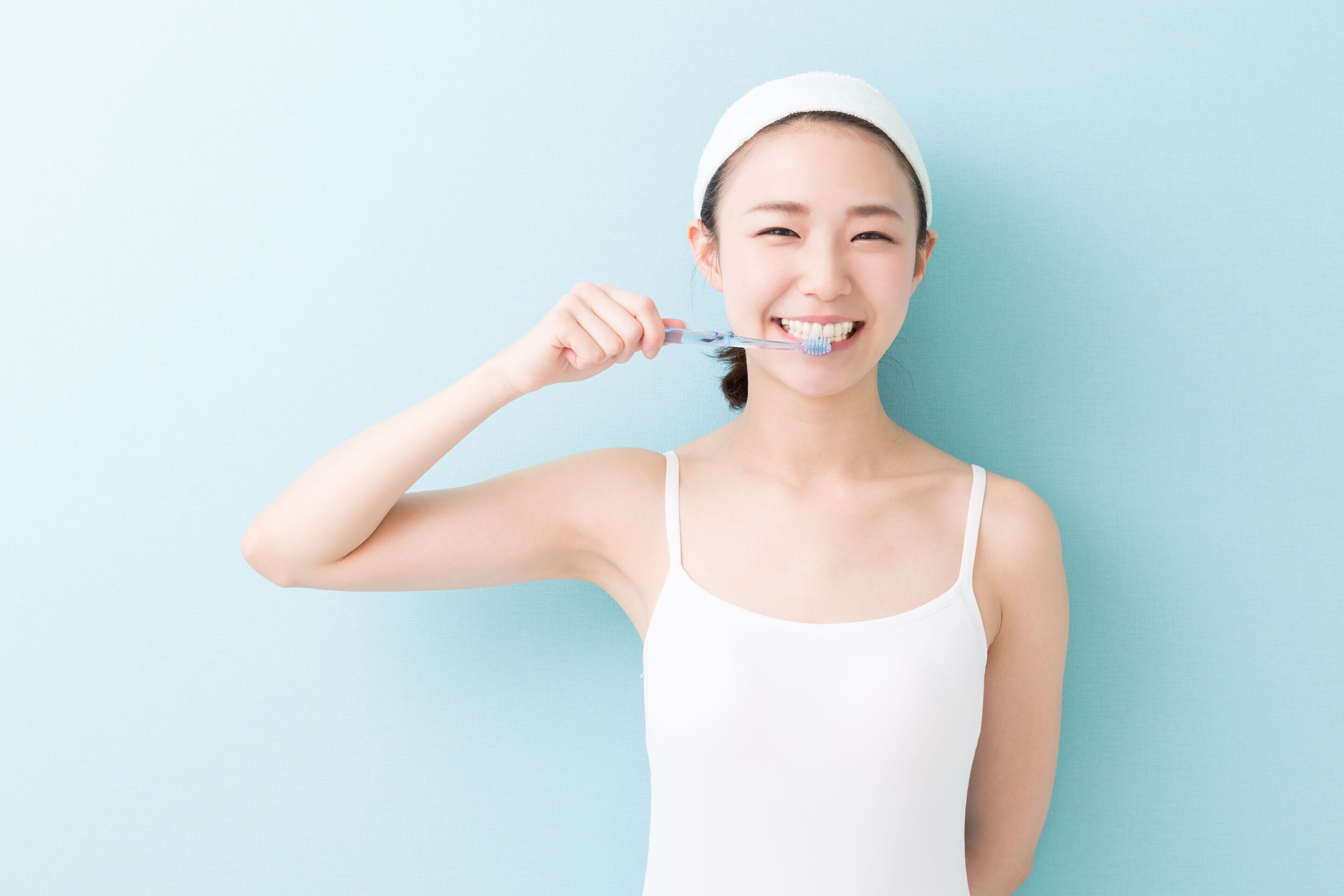 Young Asian woman in white tank top brushing her teeth