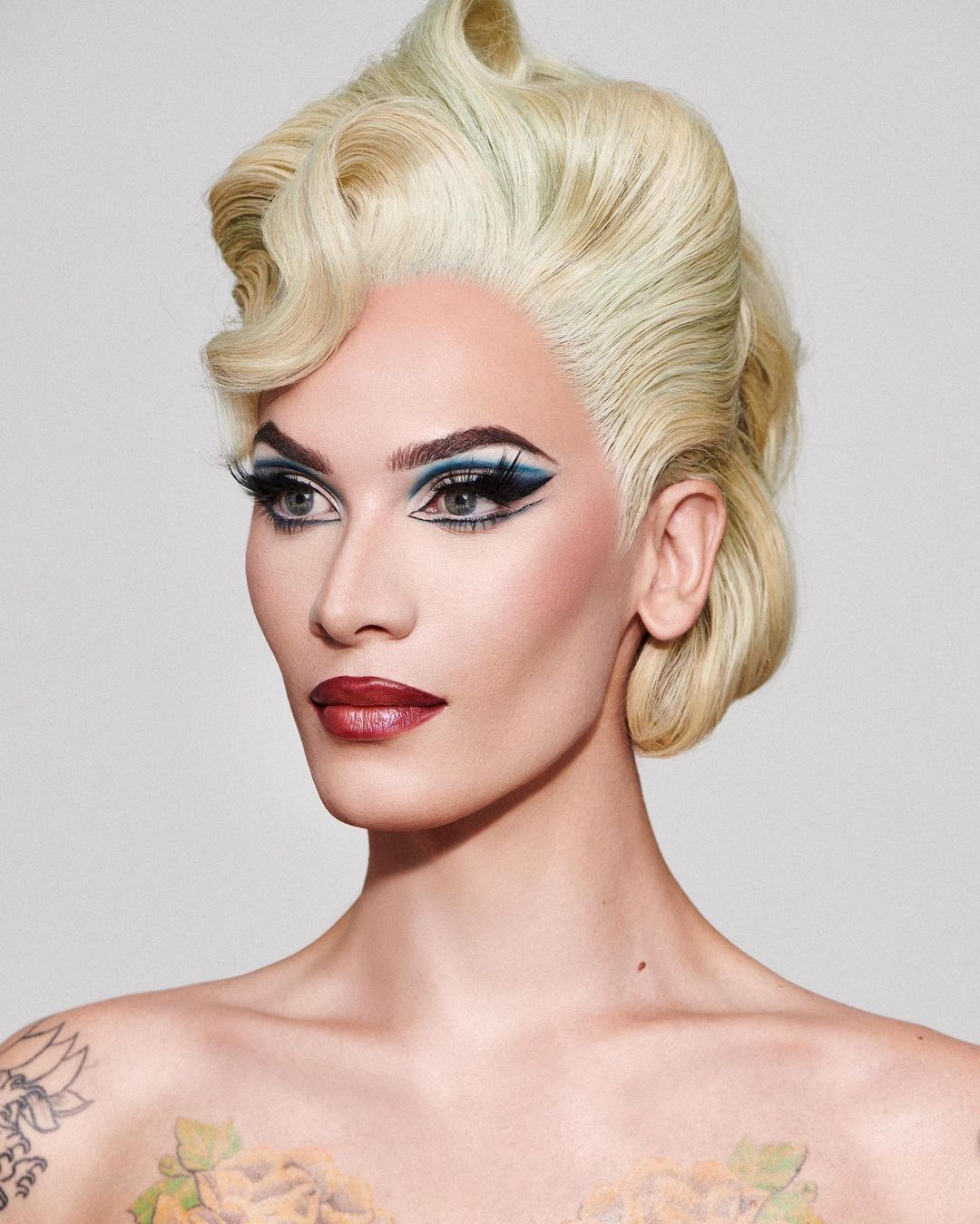 A portrait of drag queen with blue eye makeup, graphic eyeliner, and blonde updo.