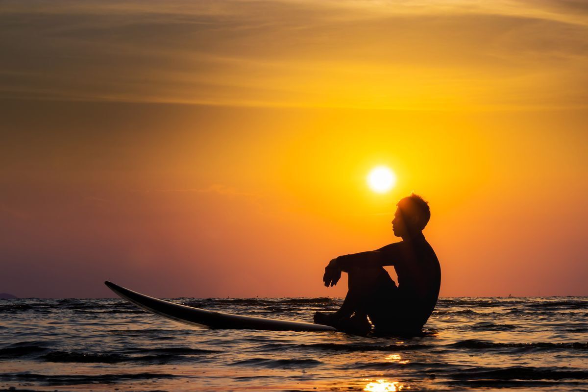 A man sitting on his surfboard looking at the open water.  