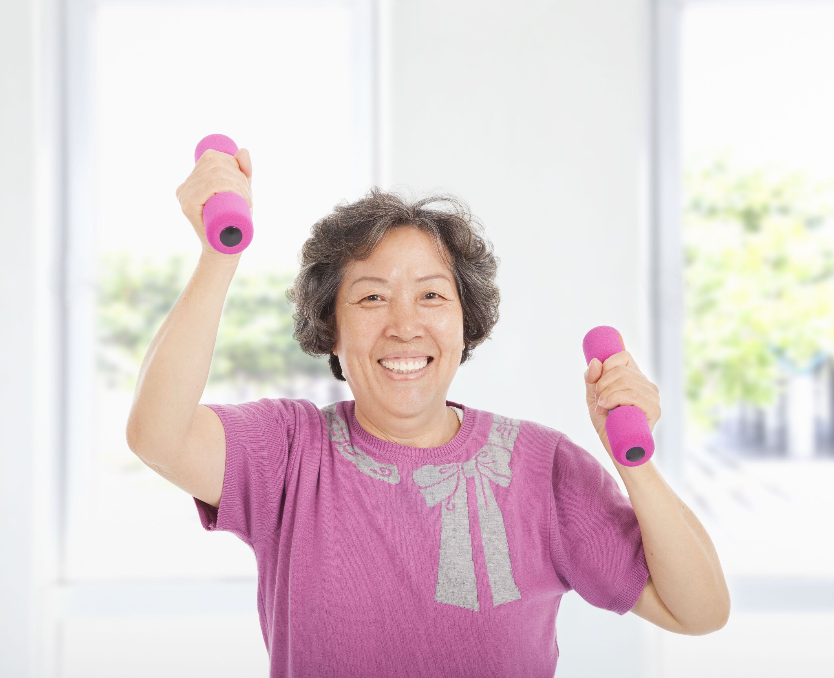 An older woman holding pink dumbbells