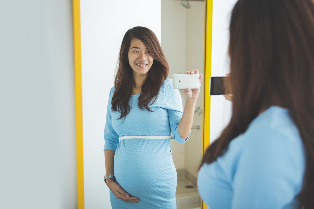 Pregnant Asian woman taking a mirror selfie