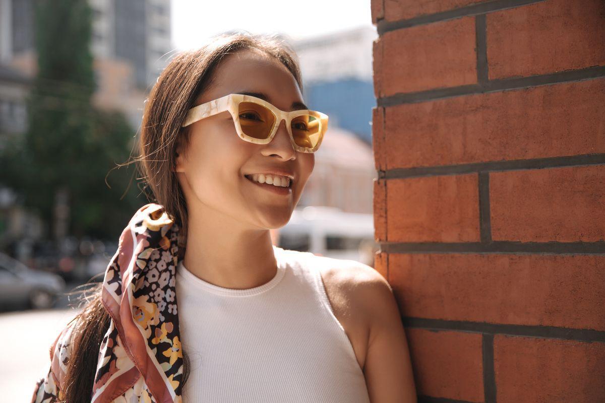 Asian woman wearing sunglasses and a silk scarf.