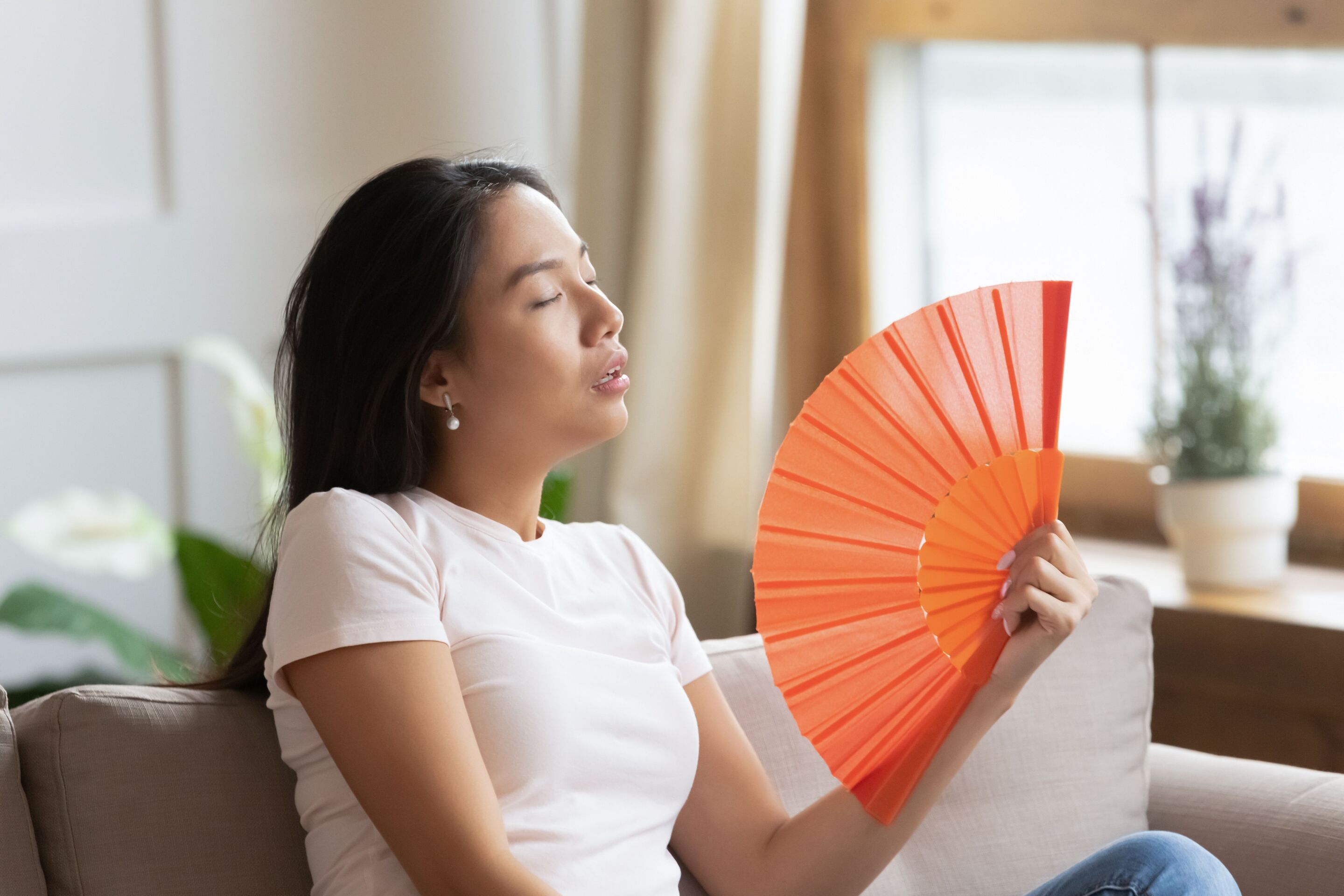 A woman fanning herself with an orange hand held fan
