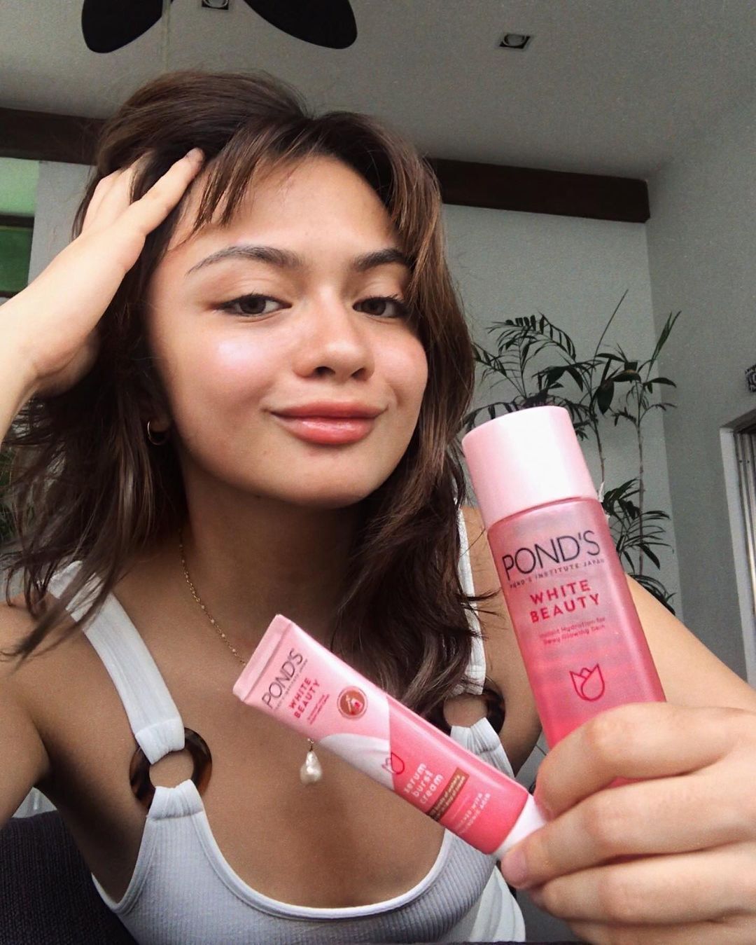 A sporty woman in a white tank top holding two POND’S White Beauty products