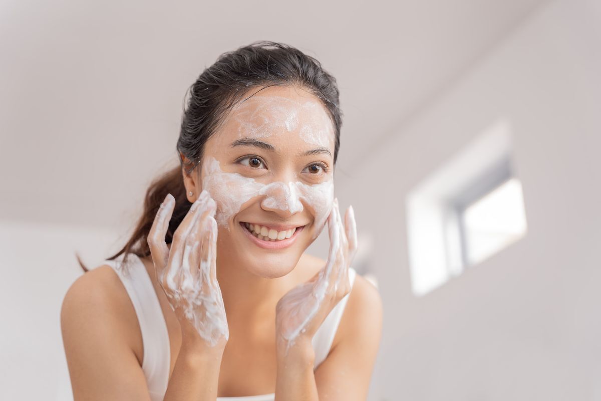 Filipino woman smiling while washing her face in the mirror