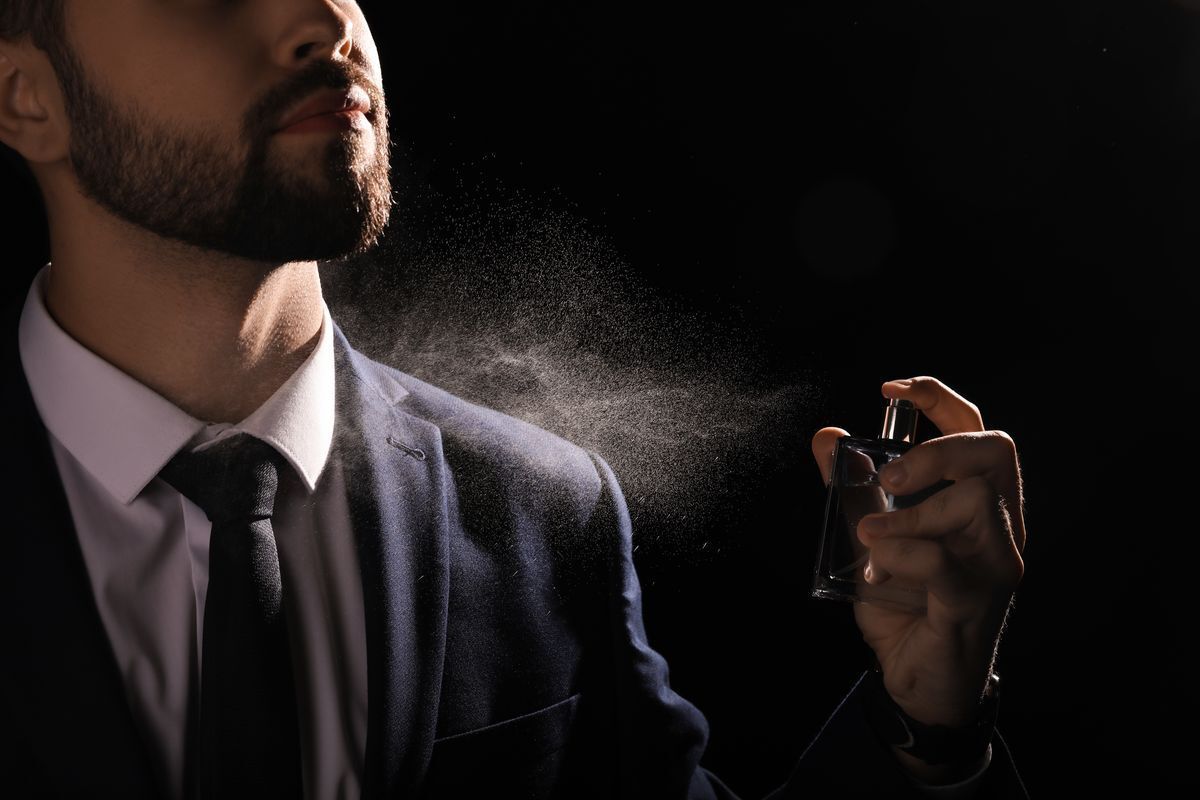 Bearded man spraying perfume on his white shirt and black suit and tie