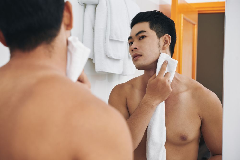 A man drying his face in front of the mirror.