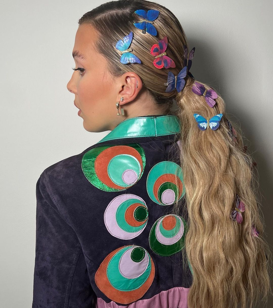 A portrait of Millie Bobby Brown with low ponytail and butterfly hair clips.