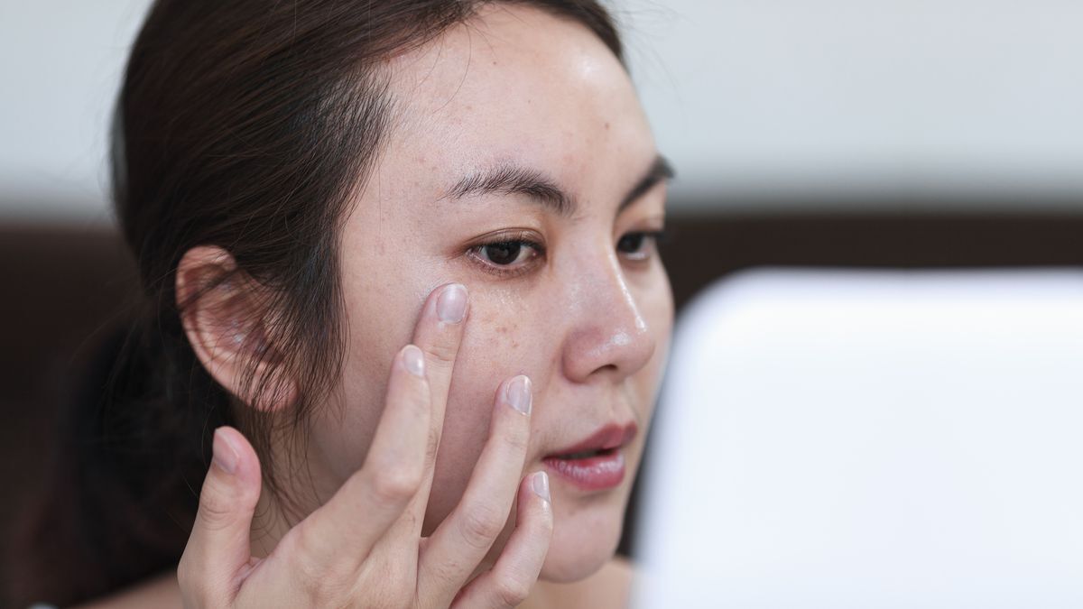 Closeup of an Asian woman applying eye cream.