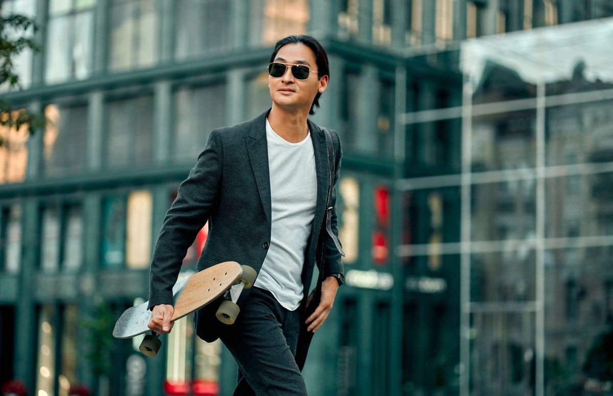 A man with black sunglasses holding a skateboard while walking across the street.