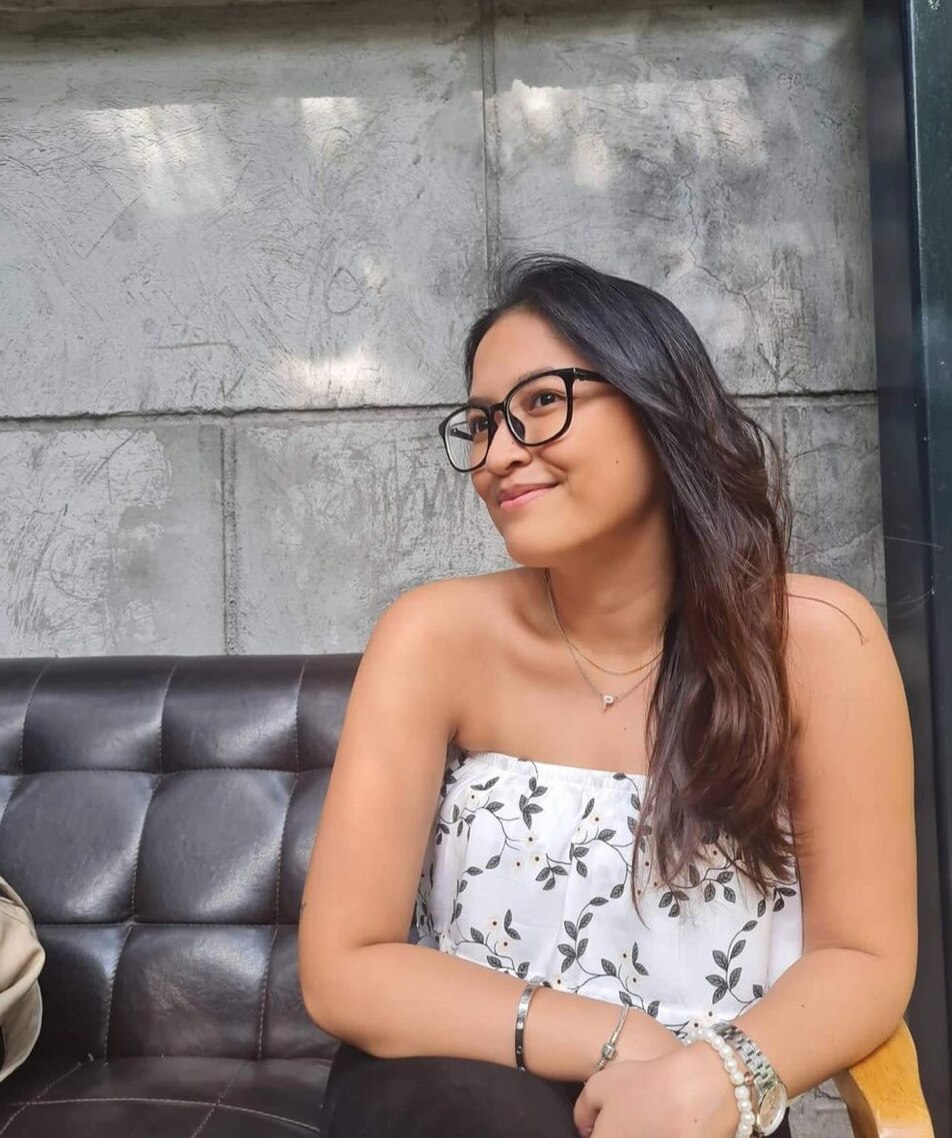 Filipino woman with glasses and long hair wearing a floral top.