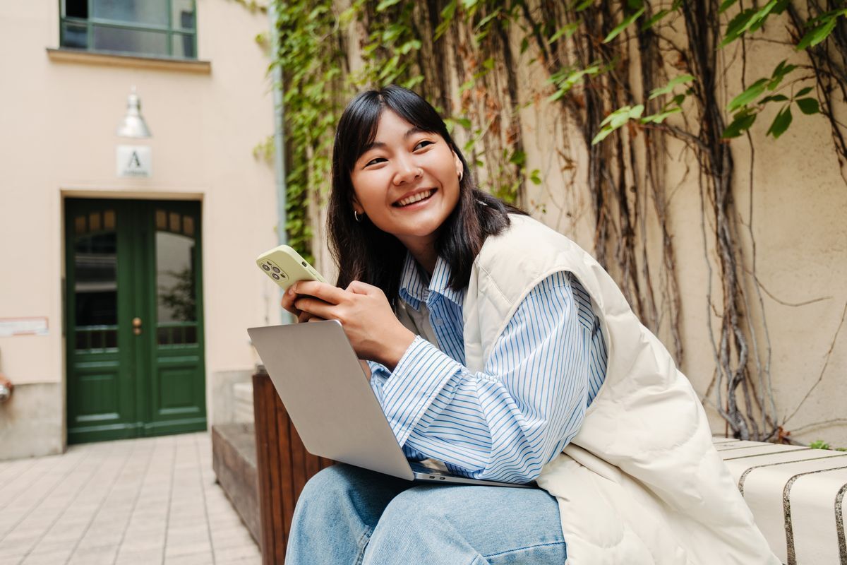 Young Asian girl holding her phone and laptop.