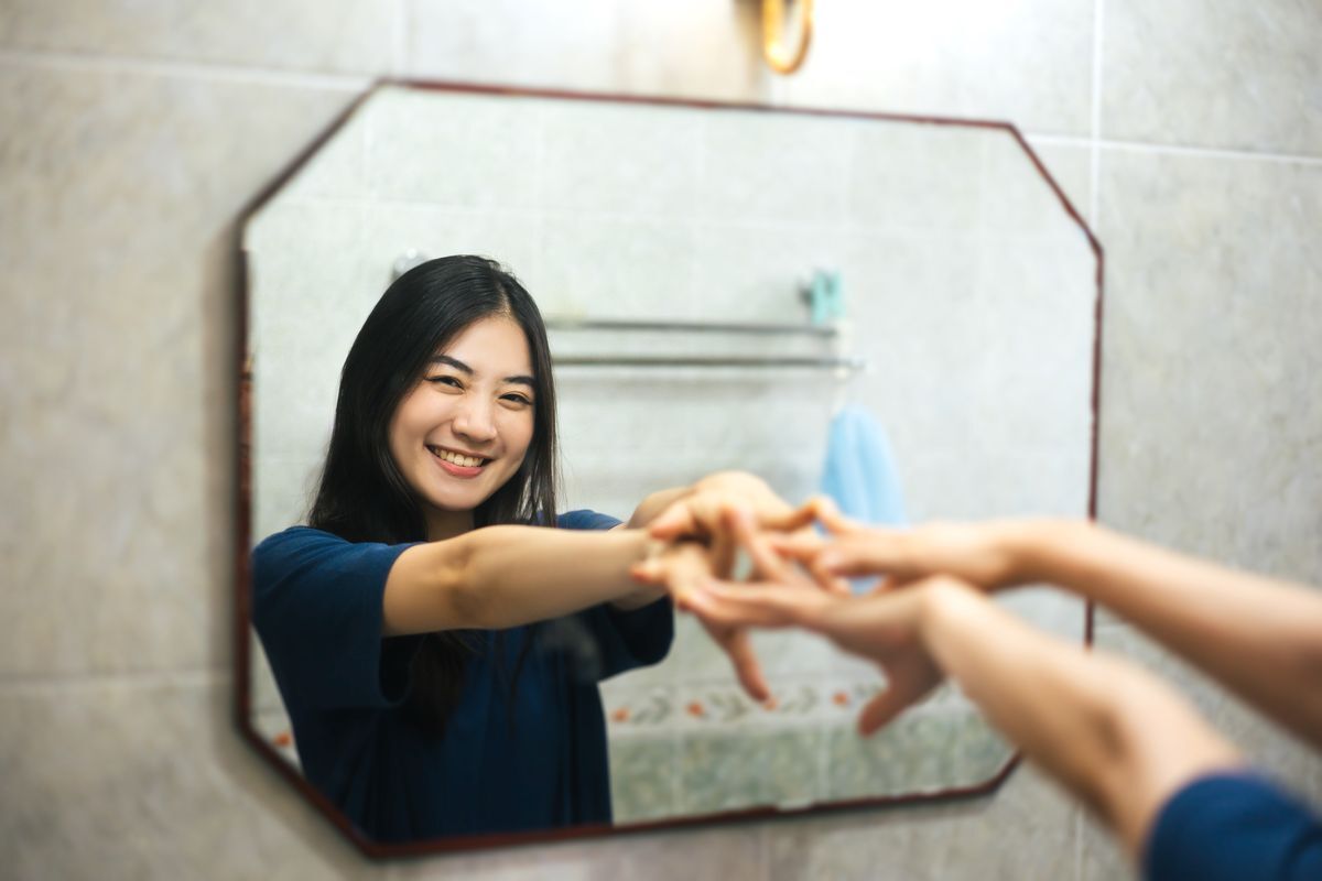 Asian girl smiling at her reflection in a mirror. 