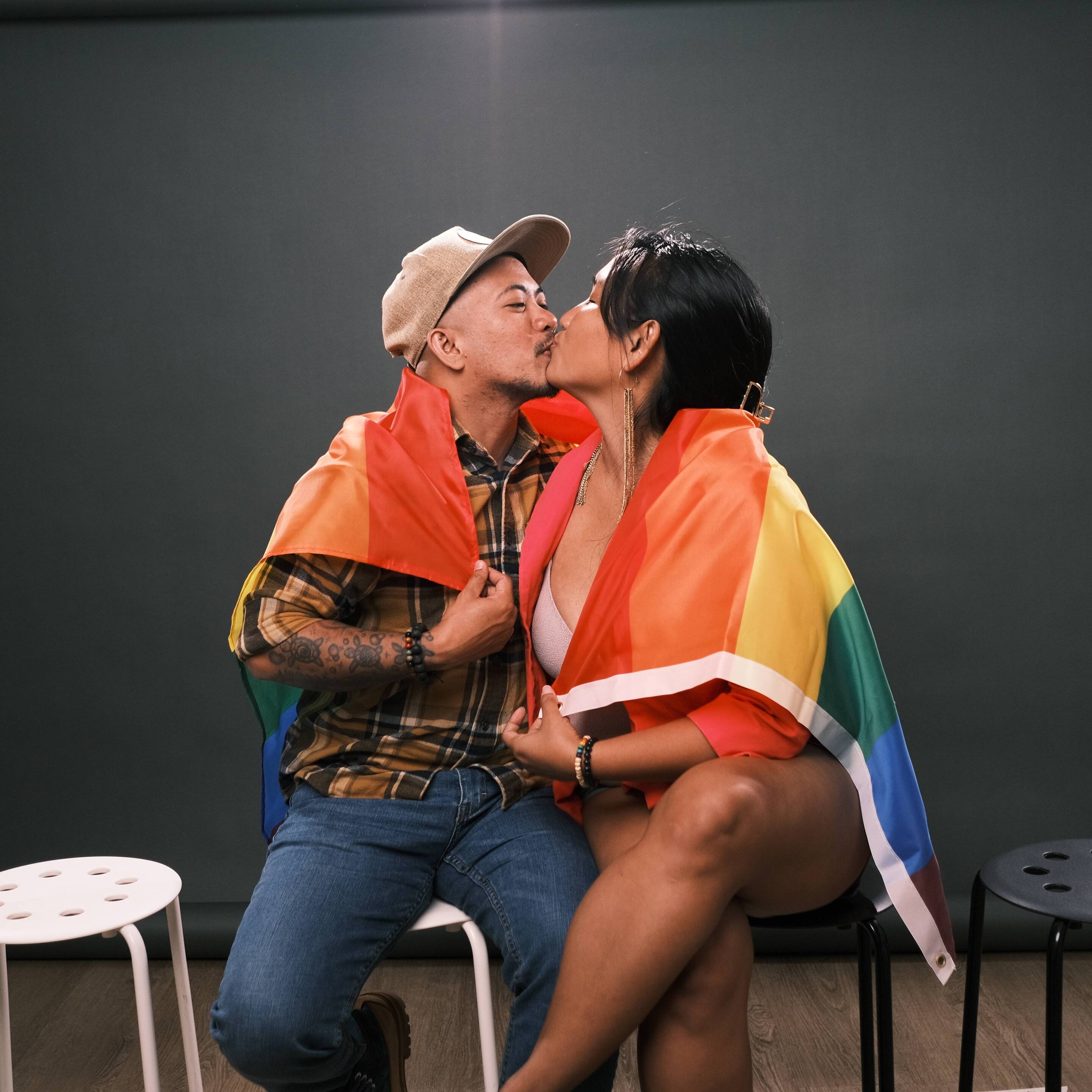 Woman and transman kissing while wrapped in the Pride flag.