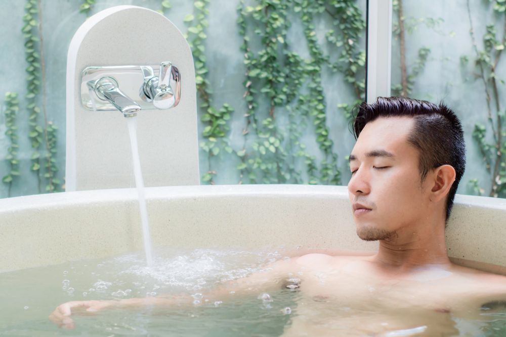 A young Asian man relaxing in the bathtub.