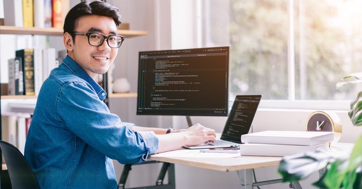 Asian man smiling with code flashed on computer screen.