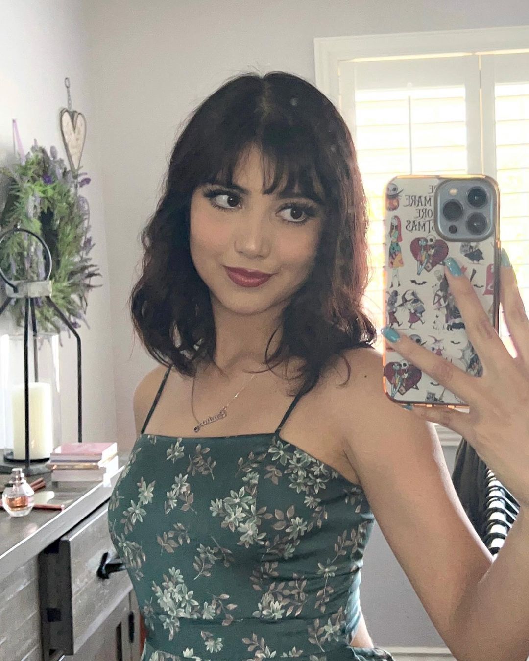 Woman with shoulder-length and wispy bangs taking a mirror selfie.