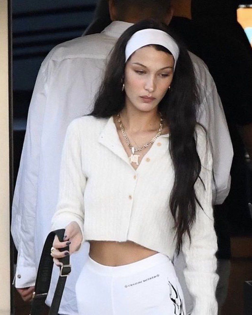 Bella Hadid stepping out of a venue with a white cardigan, biker shorts, and headband.