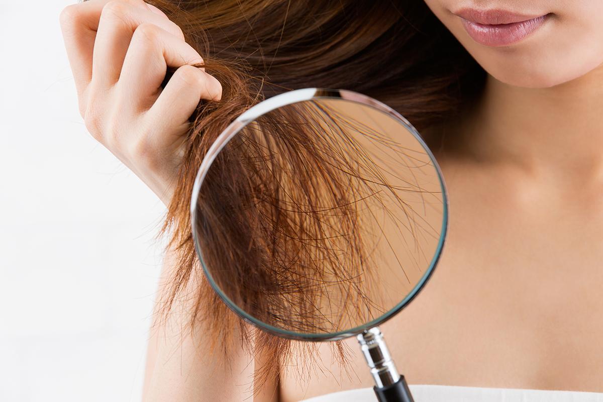 Asian woman looks at hair through a magnifying glass