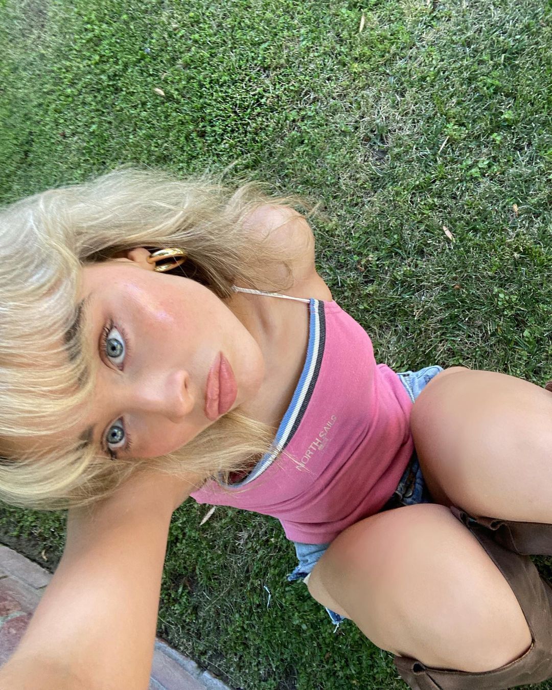  Blonde woman with dark eyebrows wearing pink tank top and jeans shorts.