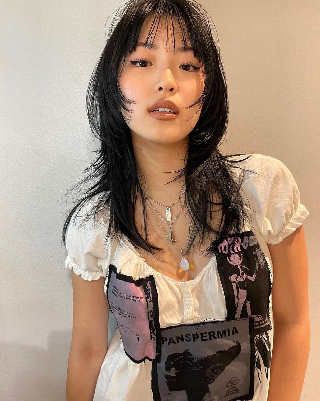 Woman with black wolf cut and thin eyebrows. 