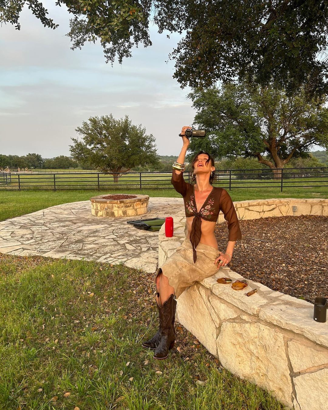 Bella Hadid in cowboy boots looking at a camcorder.