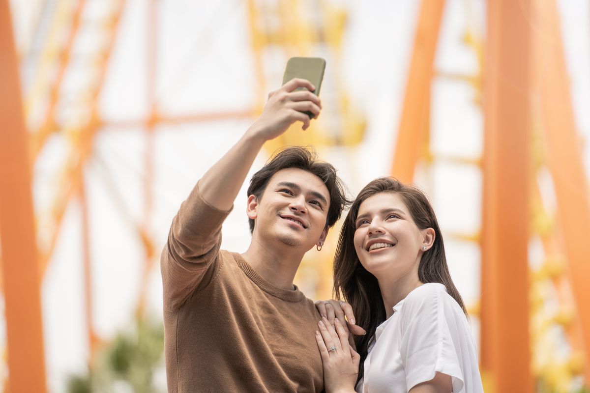 Asian couple taking a selfie by a rollercoaster.