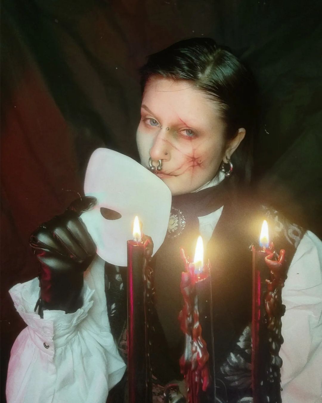 A woman dressed up as Phantom of the Opera holding a half-face white mask.