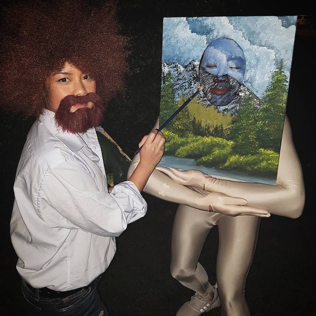 A woman dressed up as Bob Ross pretending to paint on a canvas.