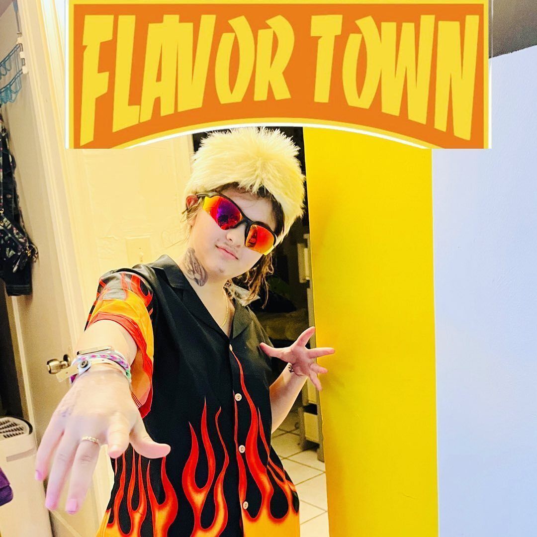 A woman dressed up as Guy Fieri with tinted sunglasses and flame shirt.