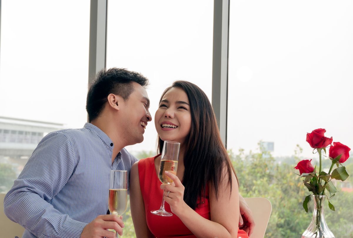 Asian man and woman laughing while on a romantic date and holding champagne.