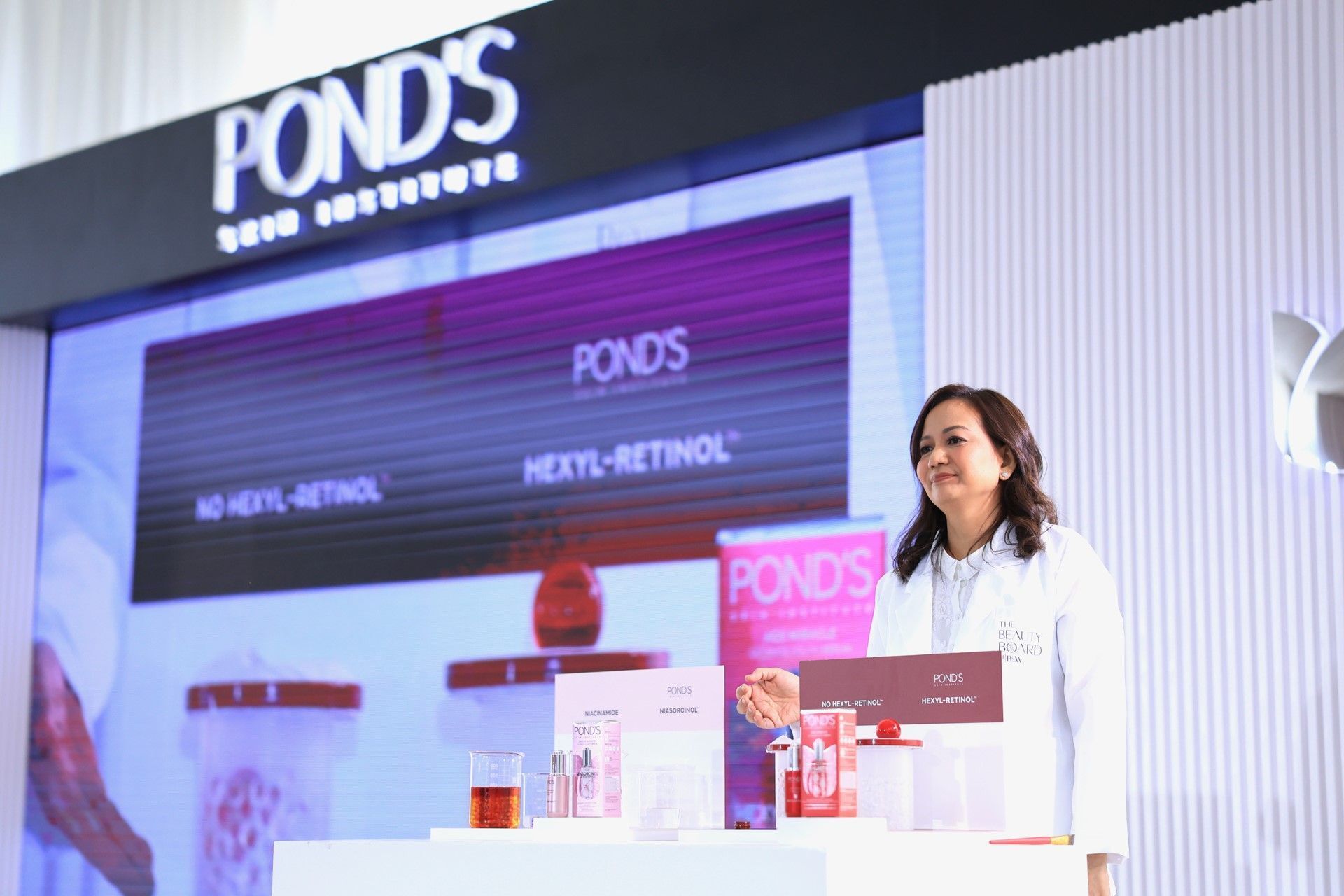 A woman showcasing skincare products on a stage.