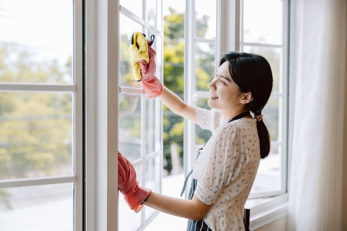 Smiling woman in dress cleaning windows with yellow rags.
