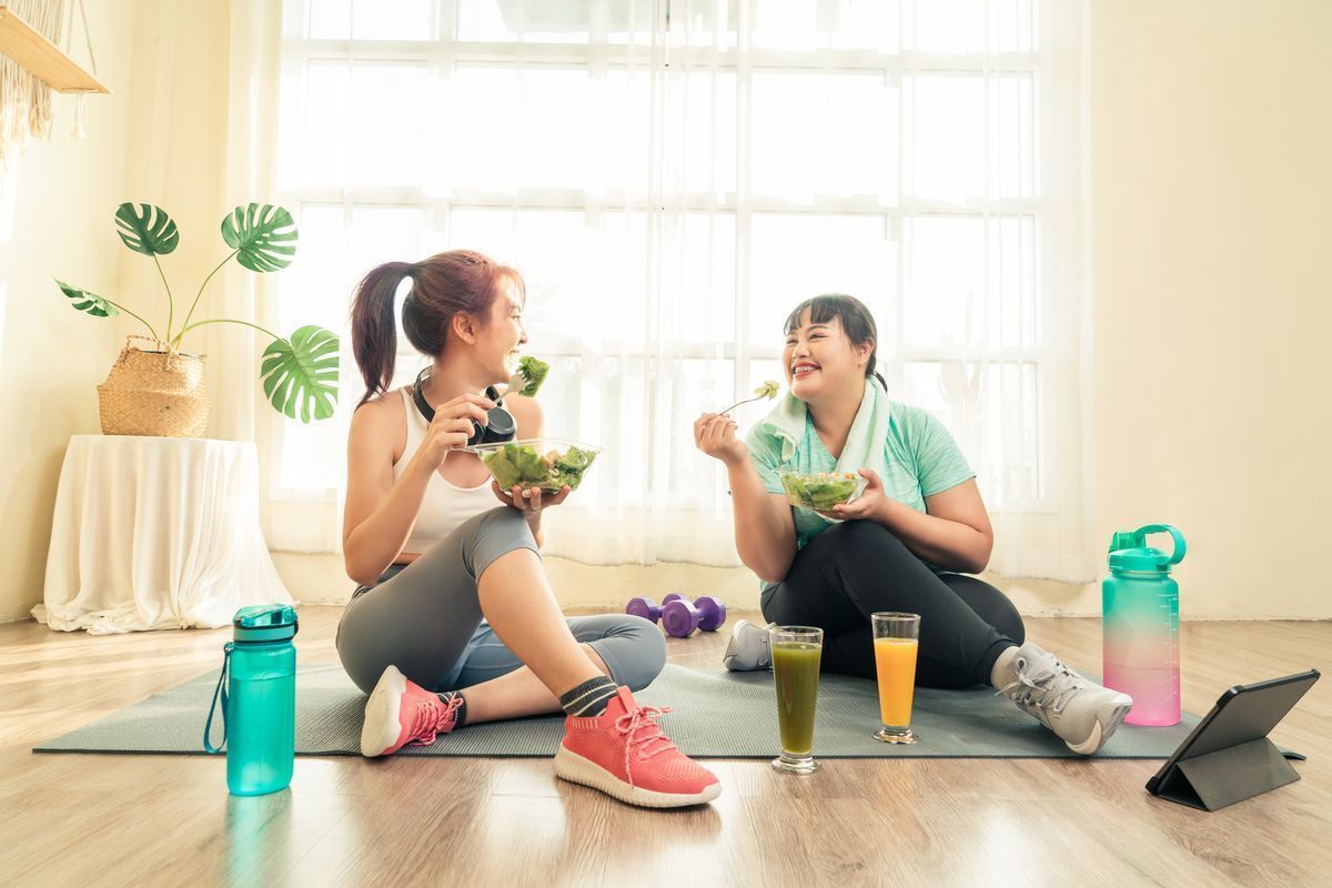 Asian friend eating salads while on yoga mat.