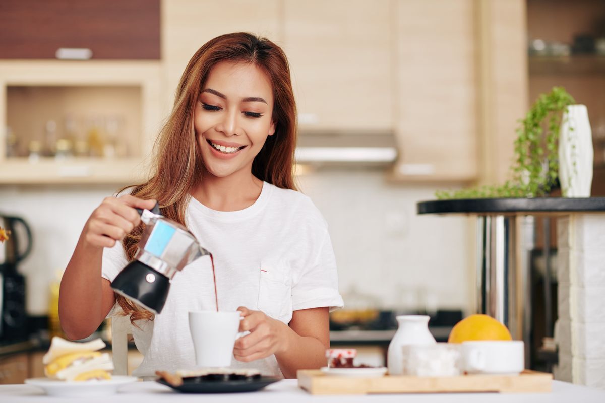 A smiling woman pouring coffee out of a Moka pot.
