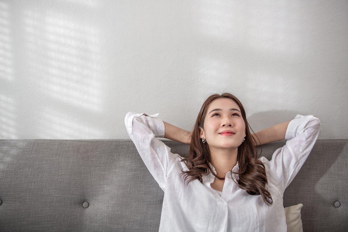 Asian woman in white shirt leaning against gray couch