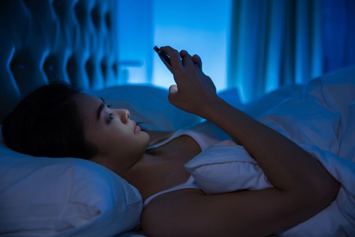 Filipino woman lying in bed before bedtime, staring at her phone screen.