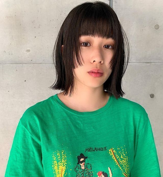 Woman wearing green shirt showing off her short hime cut with blunt bangs.