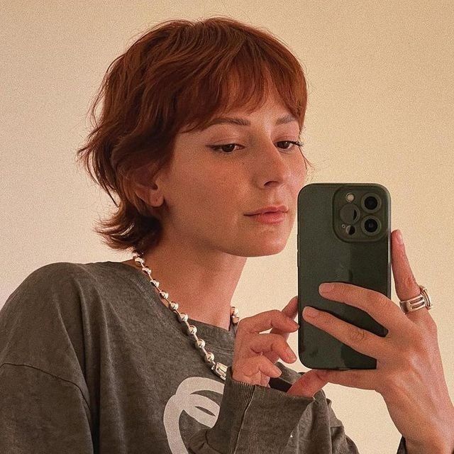 Woman with red mixie hair taking a mirror selfie.