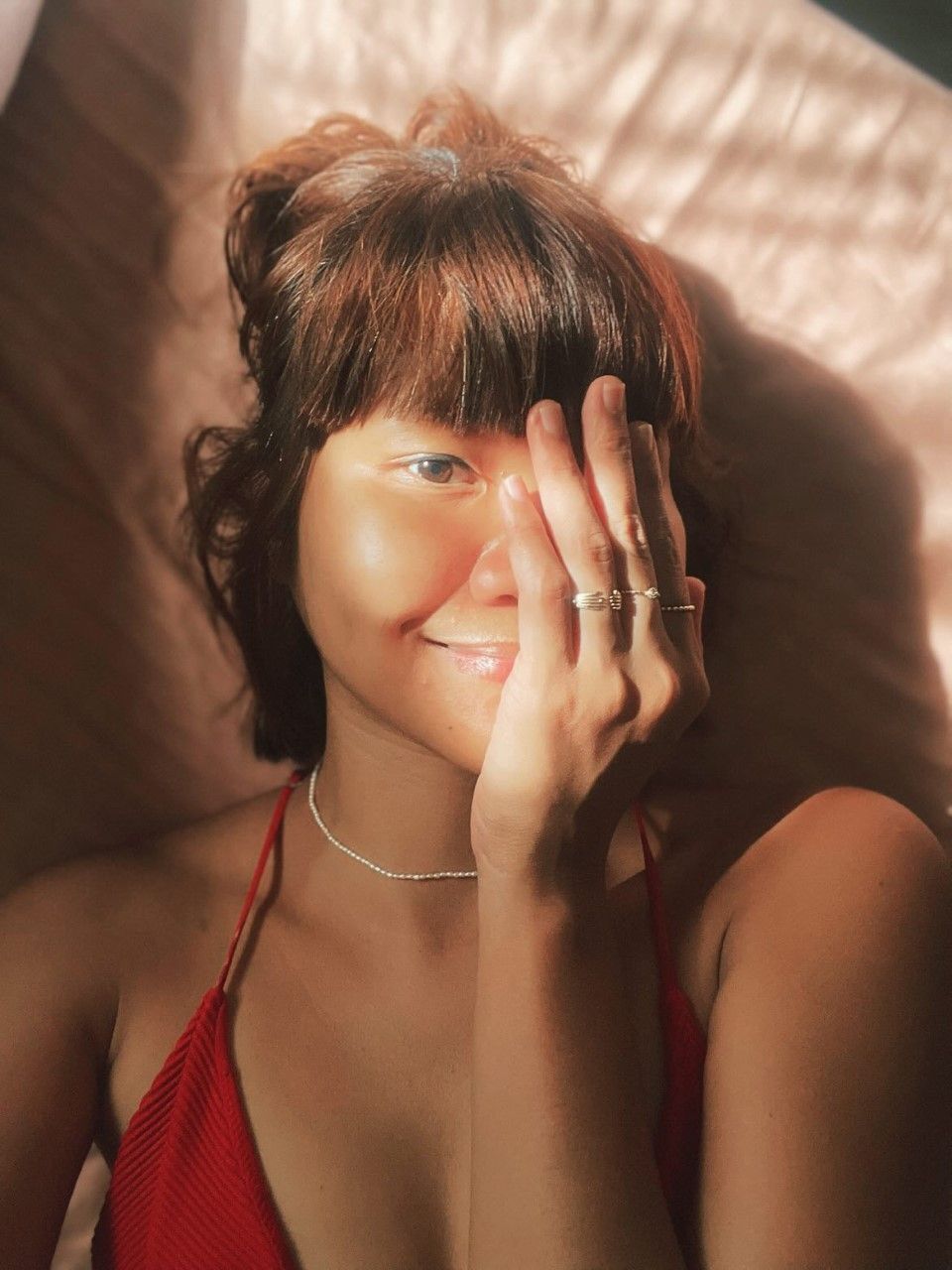 Sun lit photo of an Asian woman with bangs wearing a red top