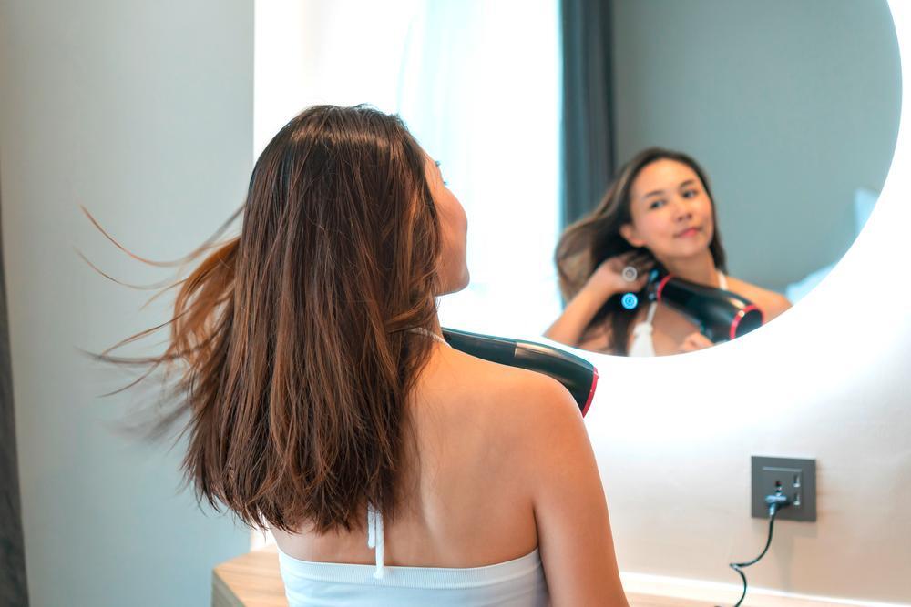 Woman using a blow dryer to dry her hair in front of a mirror.