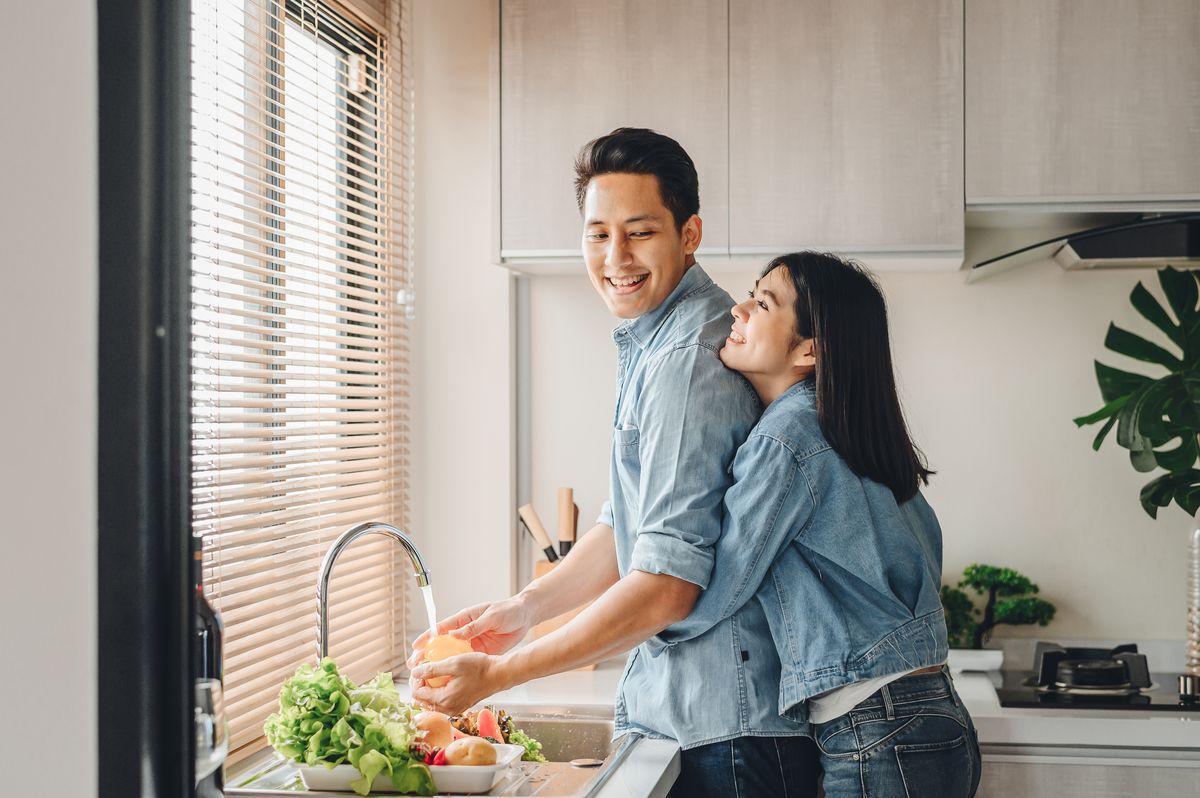 Asian couple in denim hugging while washing vegetables