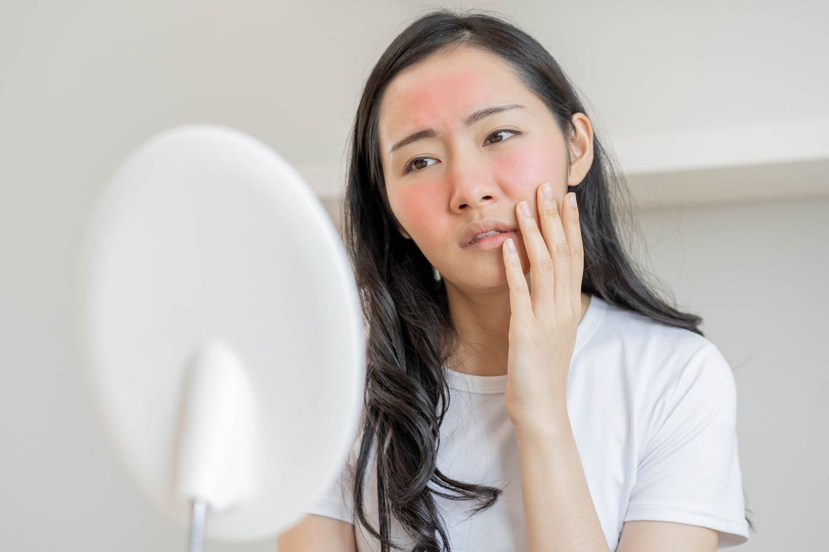 Asian woman looking at her irritated skin in a mirror.