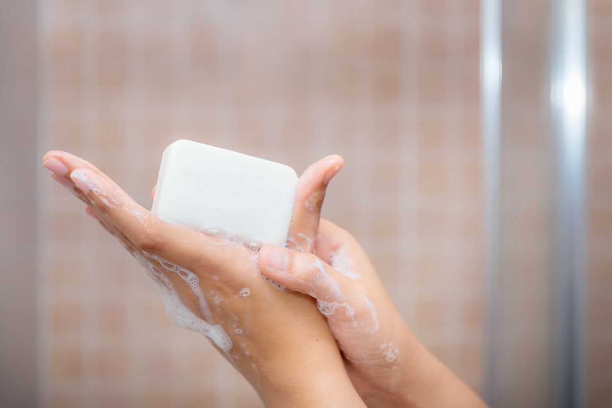 Hands holding soap with bubbles in the shower.
