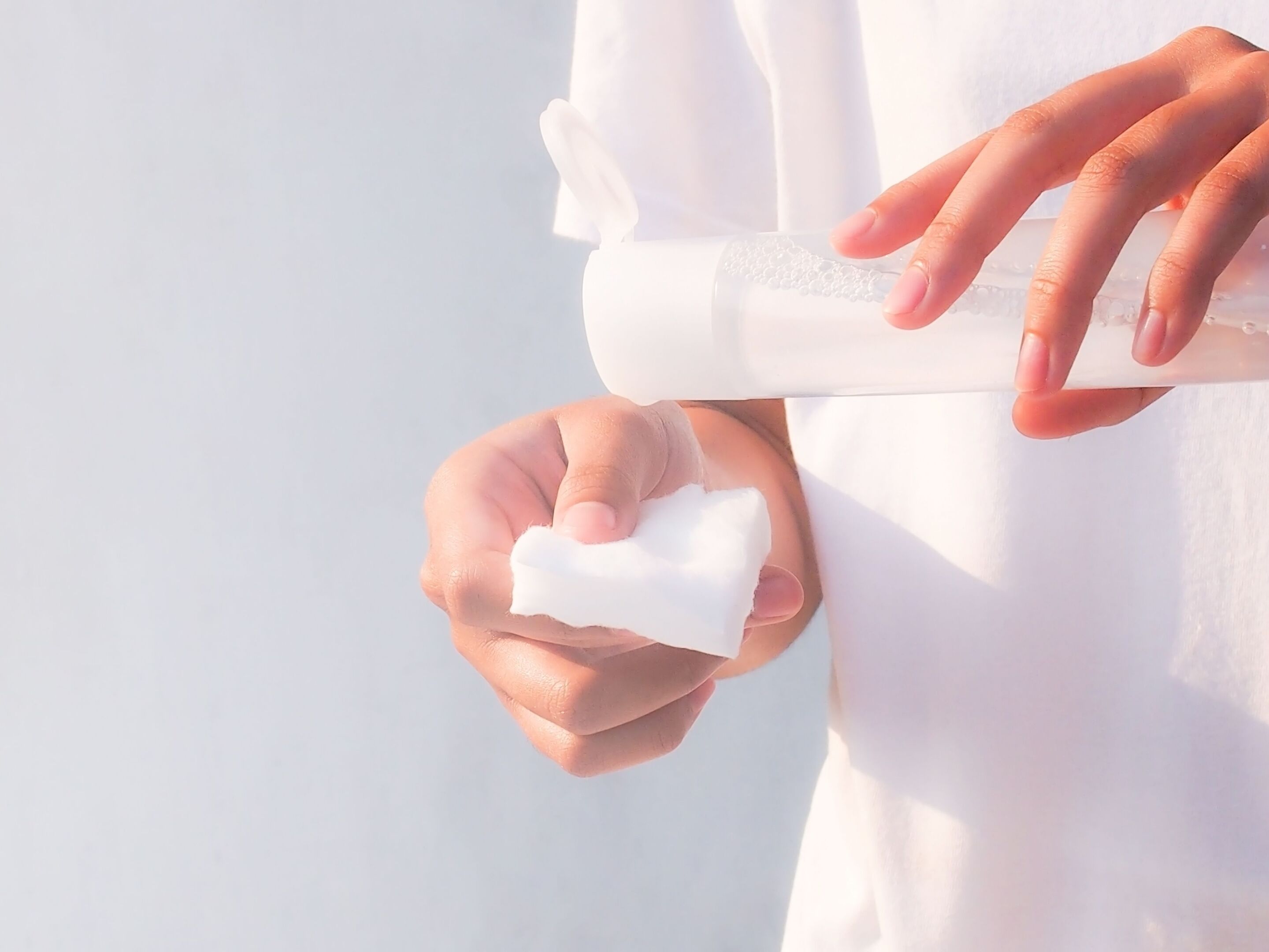 Closeup of a woman’s hand pouring toner into a cotton pad. 