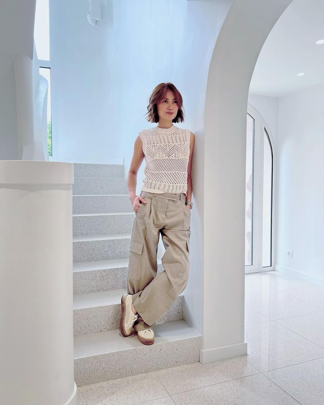 Asian woman in knits and cargo pants in a white room.