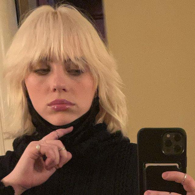 Blonde woman with a short wolf cut taking a mirror selfie