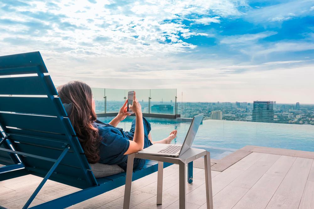 Asian woman working with a phone and laptop beside a pool.